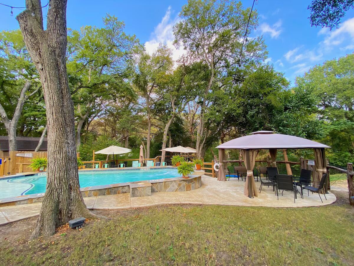 Un patio trasero con piscina, mobiliario exterior y un pabellón.