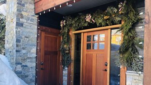 A wooden door with a stone wall, a snow-covered entrance, and a wreath with pine branches. - Amazing Upgraded Chalet with Everything You Need and It's ALL Yours - No Suite (Silver Star Mountain)