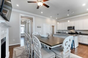 A modern kitchen with white cabinetry, a wooden dining table, and a ceiling fan.