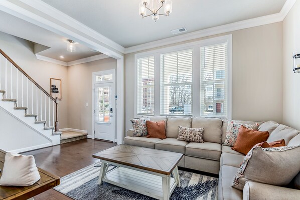 A spacious living room with a beige sofa, a coffee table, and a staircase.