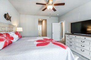 Quarto com cama, ventoinha no teto, televisão e cômoda.