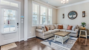 A living room with a beige sectional sofa, a wooden coffee table, and a patterned rug. - ViBe District 4BR • Walk to Virginia Beach (Virginia Beach)