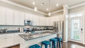 A modern kitchen with white cabinets, granite countertops, stainless steel appliances, and blue bar stools. - ViBe District 4BR • Walk to Virginia Beach (Virginia Beach)