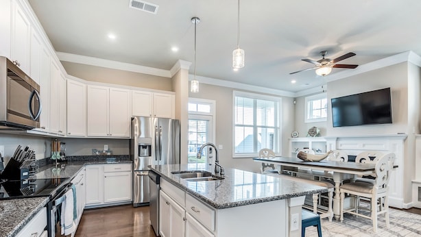 A modern kitchen with white cabinets, stainless steel appliances, a granite countertop, and a dining area with a TV and fireplace. - ViBe District 4BR • Walk to Virginia Beach (Virginia Beach)