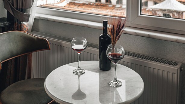 A hotel room with a round table, two wine glasses, and a bottle of wine. A chair is positioned at the table. The room features a large window with a view of buildings outside. - Pandan Karakoy Suit (Istanbul)