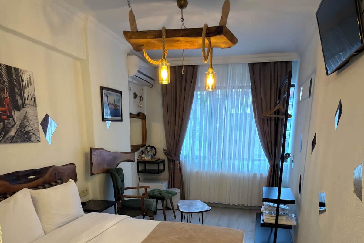 A hotel room with a large bed, a desk, a chair, a small table, a TV, and a window with curtains.