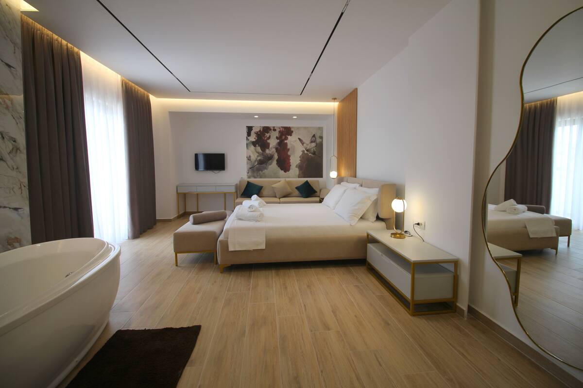 Une chambre d’hôtel moderne avec un grand lit, un coin salon, une baignoire et un grand miroir.