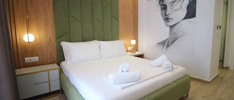 Una cama bien hecha con ropa blanca y toallas, un cabecero tapizado en verde, paneles de madera en las paredes y una lámpara fijada a la pared.