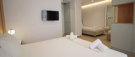 Una habitación de hotel moderna con una cama grande, un televisor de pantalla plana montado en la pared, un vestidor y un baño con ducha e inodoro.