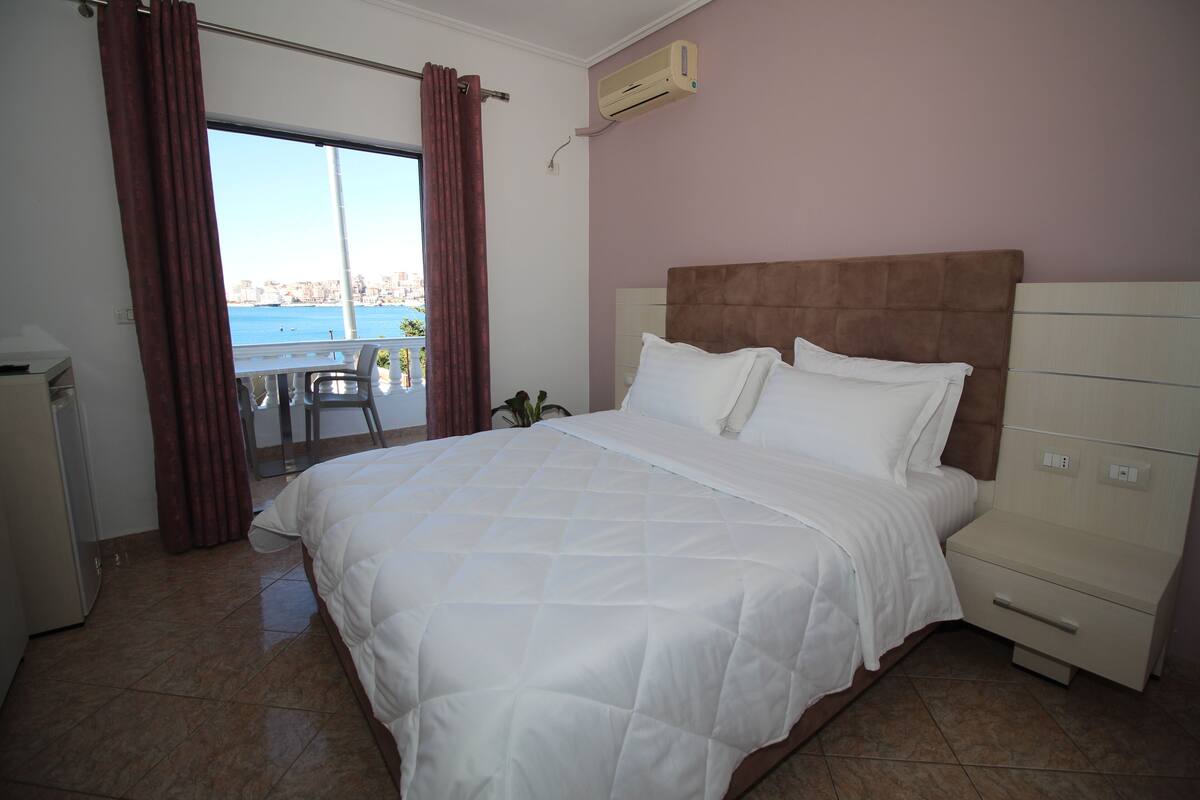 Une chambre d’hôtel avec un grand lit, une table de chevet, une chaise et une vue sur la mer.
