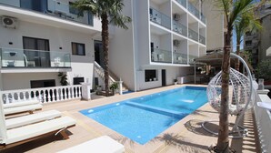 A swimming pool with lounge chairs, a palm tree, and a hanging chair. - Julia Hotel (Sarandë)