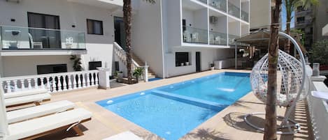 A swimming pool with lounge chairs, a palm tree, and a hanging chair.