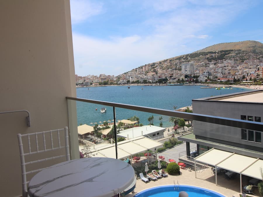 Un balcó amb vista a una ciutat costanera, una piscina i seients a l'aire lliure.