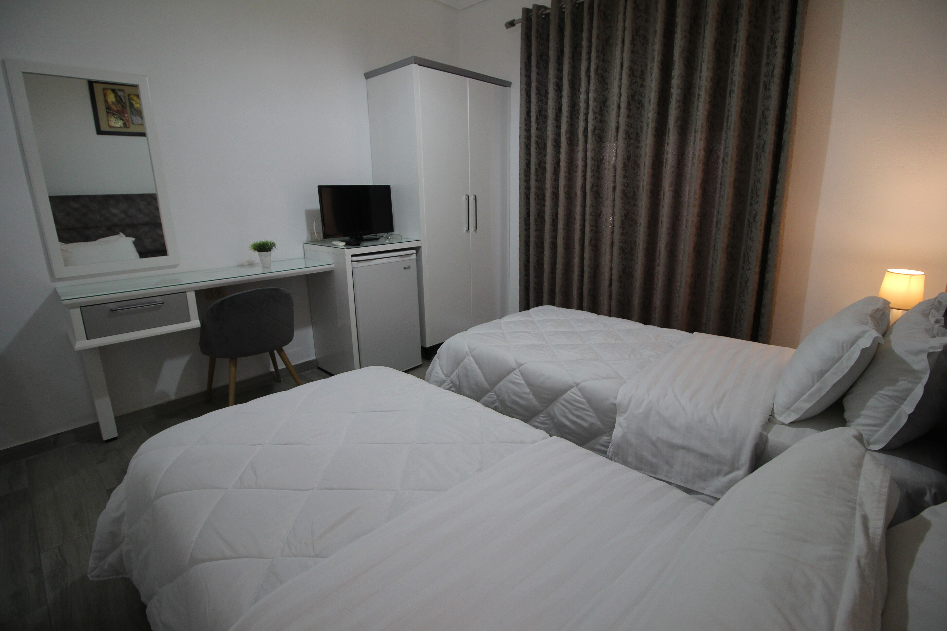 A hotel room with two beds, a desk with a computer, a chair, a wardrobe, and a curtain.