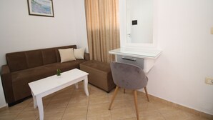 A room with a brown sofa, a white desk, a chair, a small table, and a painting on the wall. - Julia Hotel (Sarandë)