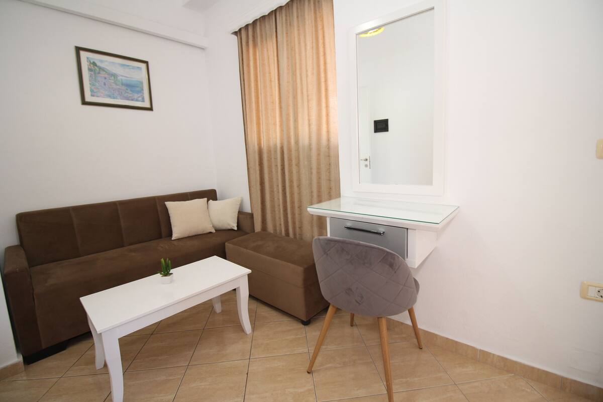 Une pièce avec un canapé marron, un bureau blanc, une chaise, une petite table et un tableau accroché au mur.