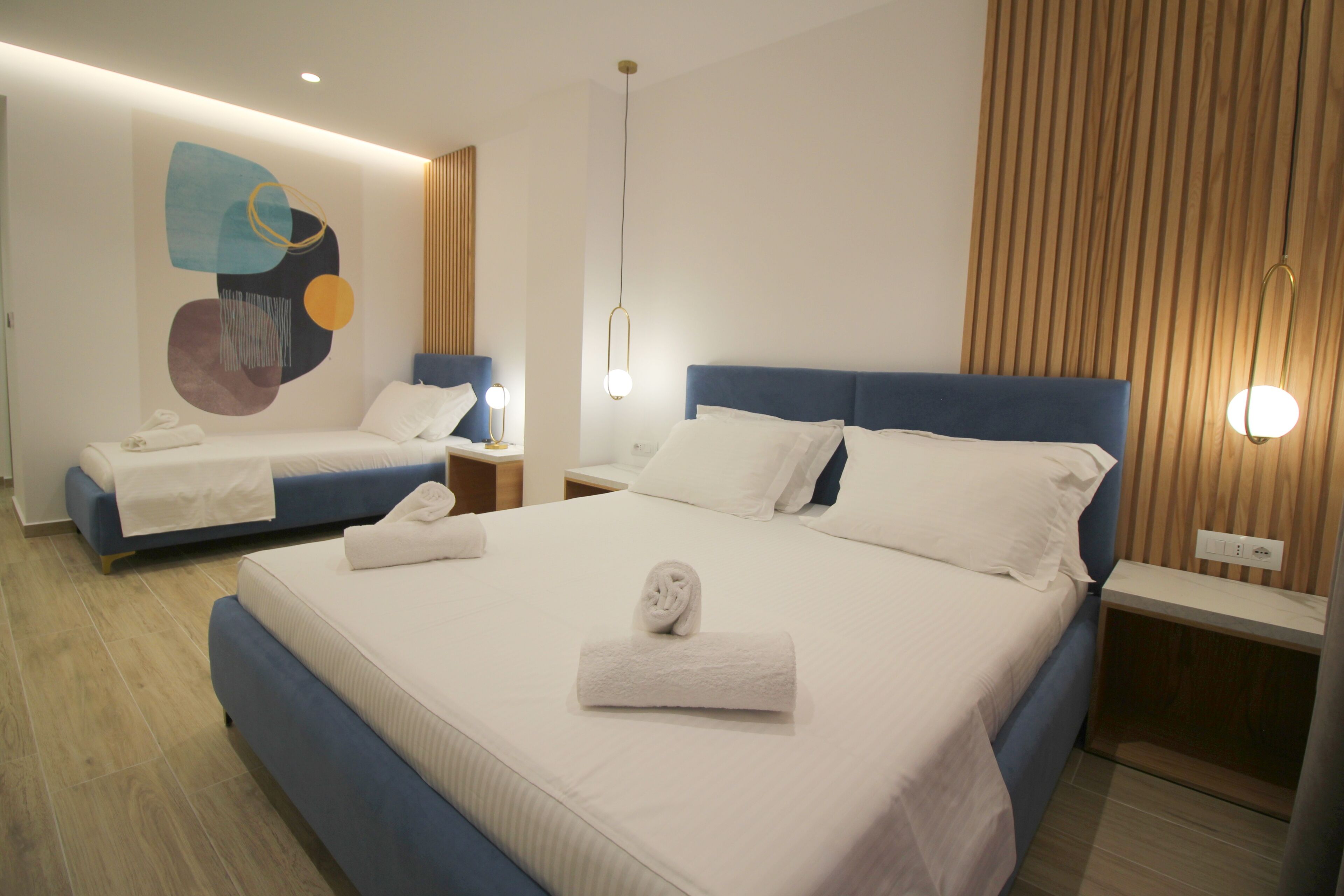 Habitación de hotel con una cama grande, una cama más pequeña, una obra de arte en la pared y un panel de madera.