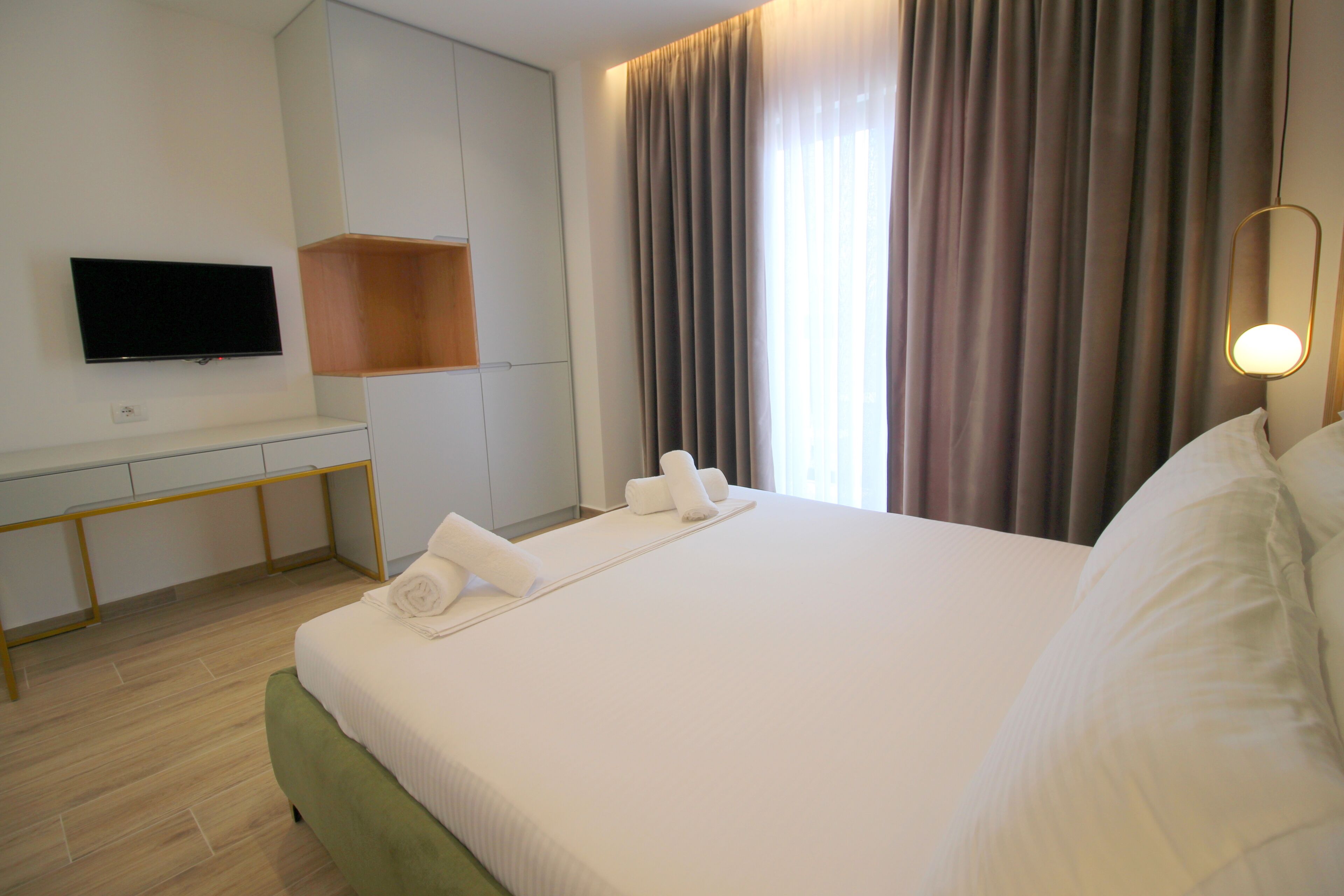 Habitació d'hotel amb un llit, una televisió penjada a la paret, escriptori i finestra amb cortines.
