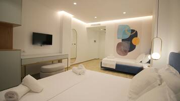 A modern hotel room with a large bed, a bedside table, a TV mounted on the wall, and a bathroom visible through an open door.