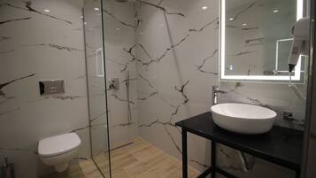 Un baño moderno con cabina de ducha de vidrio, inodoro blanco y tocador negro con lavamanos blanco.