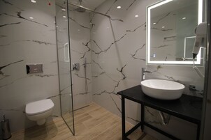 Un baño moderno con cabina de ducha de vidrio, inodoro blanco y tocador negro con lavamanos blanco.