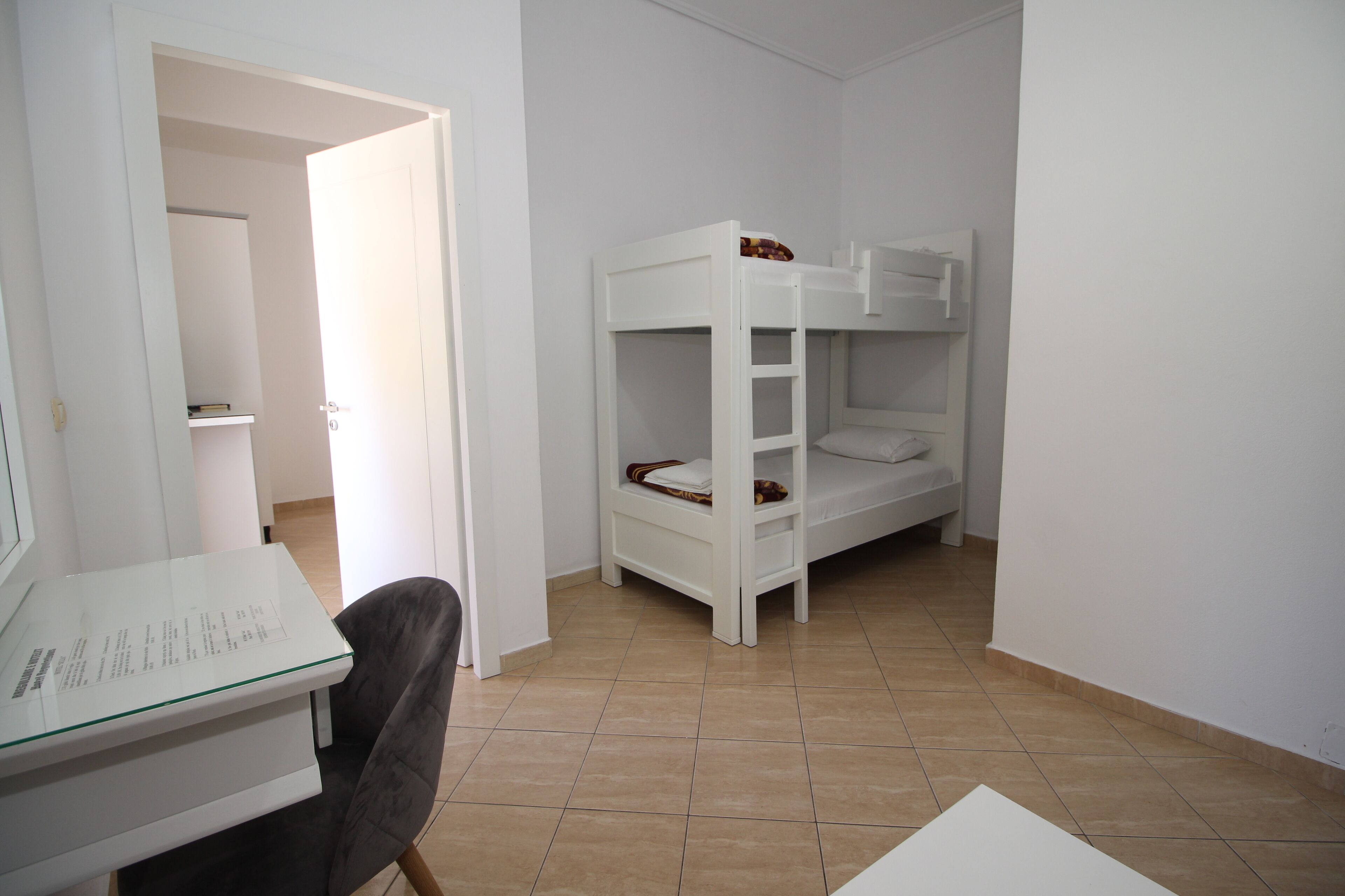 A room with a bunk bed, a desk with a chair, and a door leading to another room.