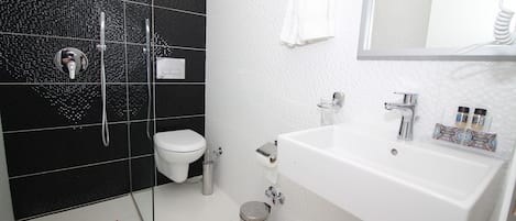 A bathroom with a white sink, a mirror, a toilet, and a shower area with black tiles.