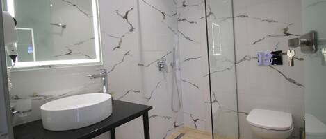 A modern bathroom with a white marble sink, a black vanity, a glass-enclosed shower, and a toilet.