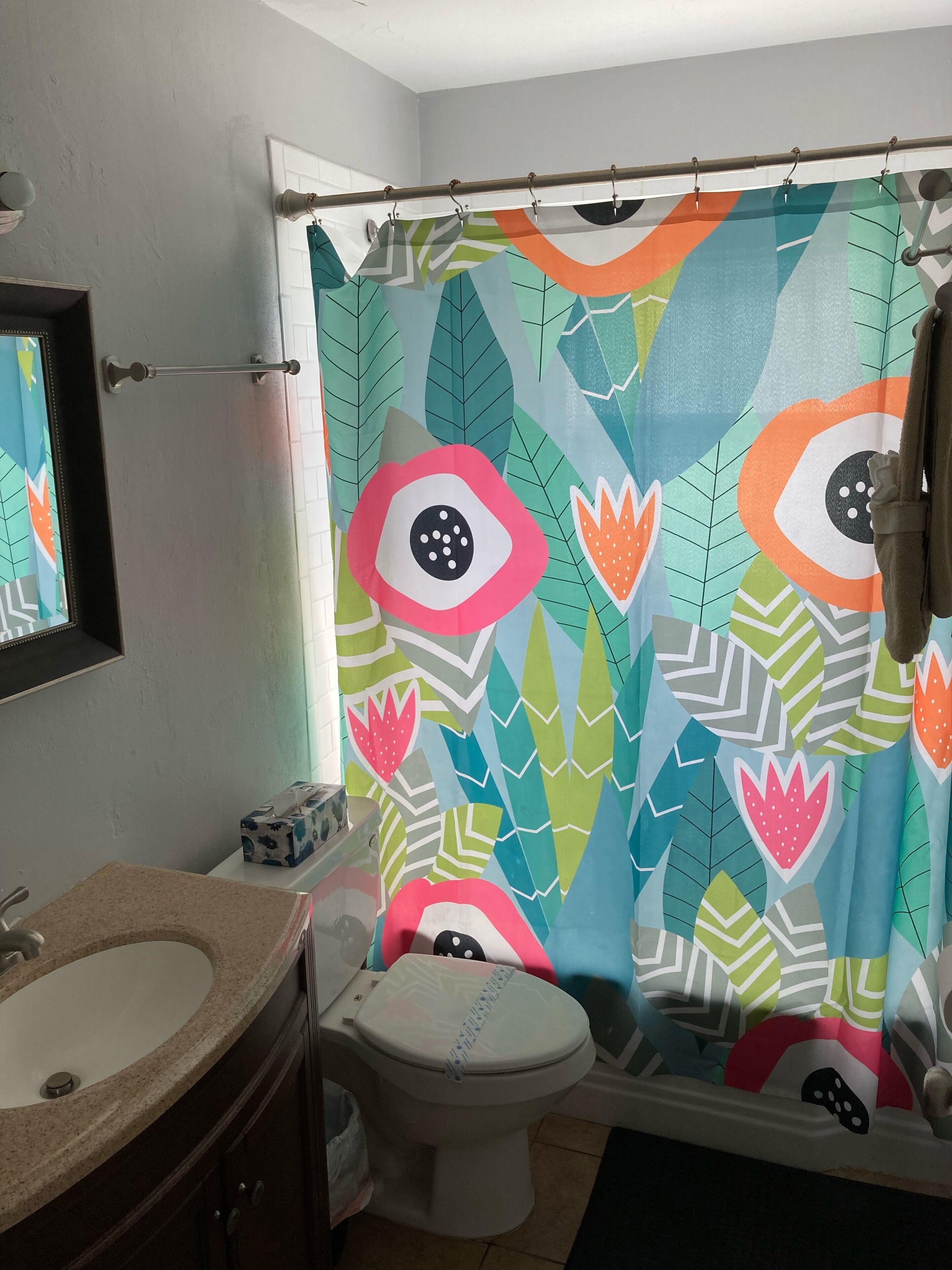 Een badkamer met douchegordijn met blad- en oogpatroon, een toilet en een wastafel met spiegel erboven.