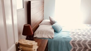 A bedroom with a wooden headboard, a bedside table with a lamp, and a bed with patterned bedding. - North Lakeland bungalow (Lakeland)