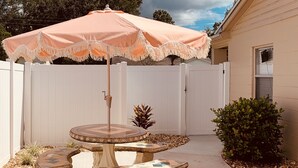 A patio with a round table and benches, an umbrella, and a white fence in the background. - North Lakeland bungalow (Lakeland)