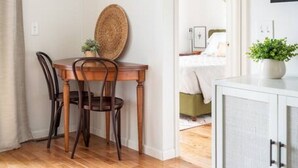 A room with a wooden dining table, two chairs, a woven basket on a shelf, a white cabinet, and a door leading to another room.