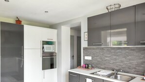 A modern kitchen with grey cabinets, a built-in oven, a microwave, and a stainless steel sink. - Homerez - House in Fort-Moville (Fort-Moville)
