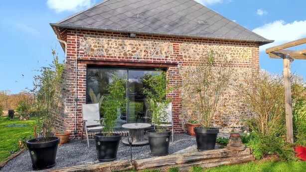 A brick building with a tiled roof, a glass door, and a patio with potted plants. - Homerez - House in Fort-Moville (Fort-Moville)