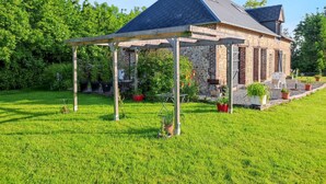 A brick building with a covered patio area, surrounded by a well-maintained lawn and potted plants. - Homerez - House in Fort-Moville (Fort-Moville)