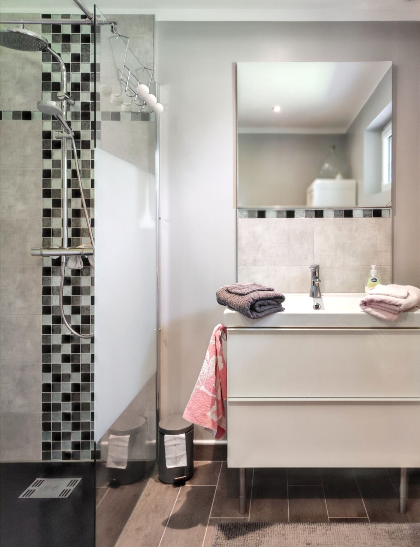 Une salle de bain moderne avec une douche à parois de verre, un meuble-lavabo blanc avec un miroir et un sol carrelé.