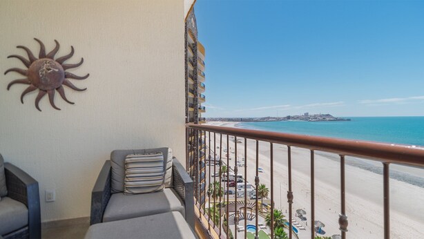 Un balcón con vista a la playa, un adorno de sol y una silla con cojín a rayas.