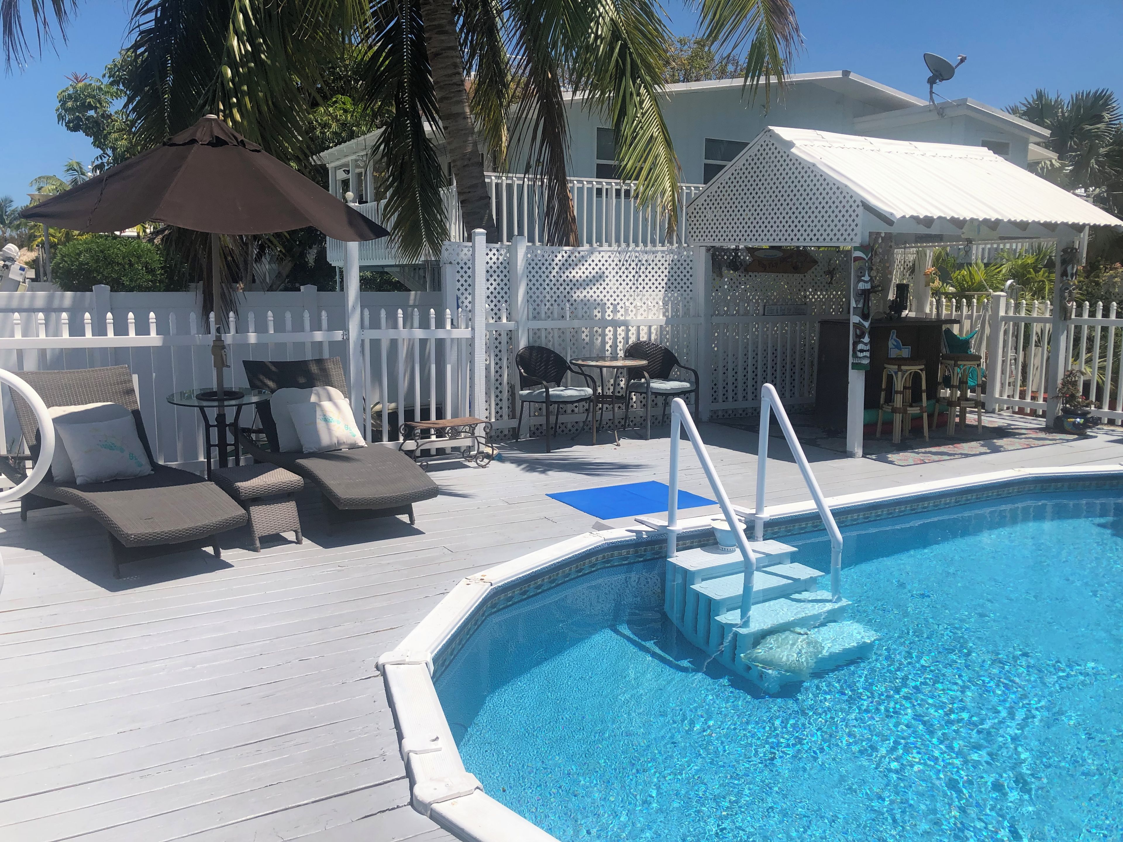 Un espace piscine comprenant des chaises longues, une table et un coin salon abrité.