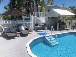 A pool area with lounge chairs, a table, and a covered seating area.