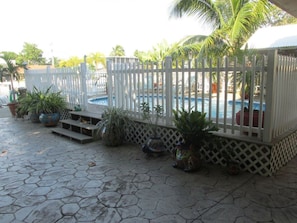 A pool area with a white fence, potted plants, and a stone-tiled floor.