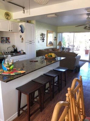 A kitchen with a central island, wooden stools, and a dining area with a sofa and chairs. - Fabulous Waterfront Pool Two Level Home  (Islamorada)