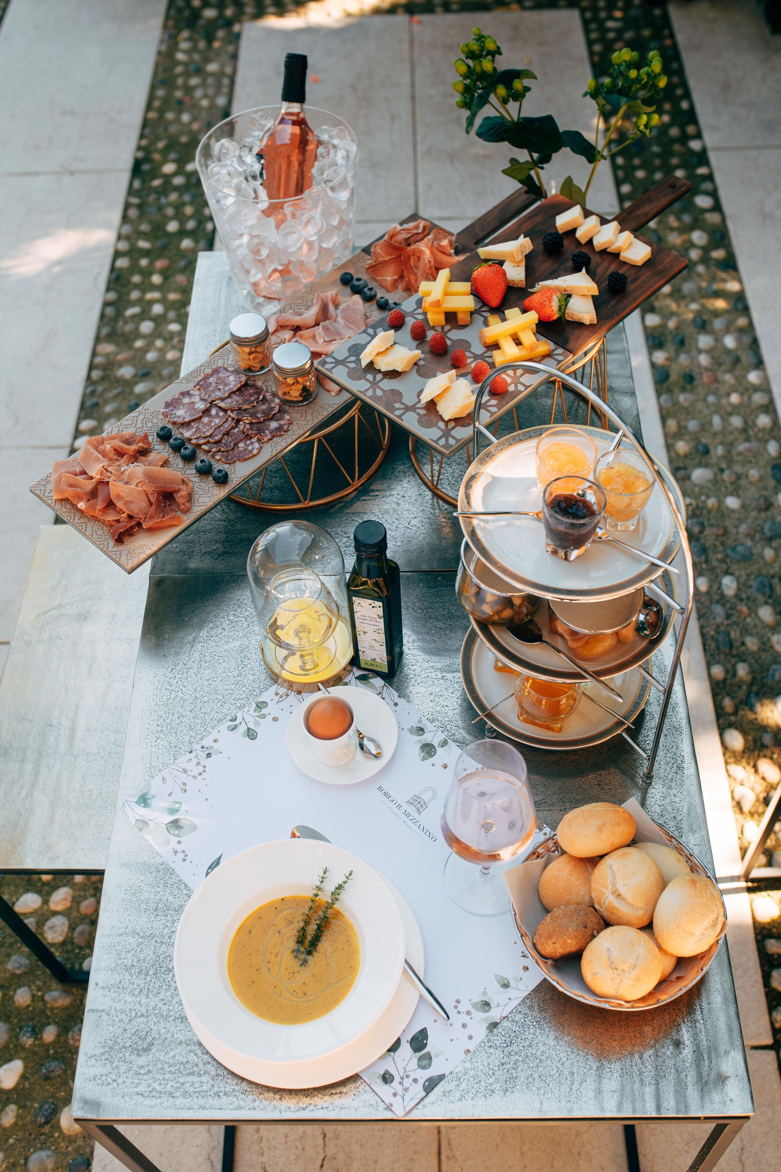 Une table dressée avec divers aliments, notamment des fromages, des viandes et du pain, ainsi que des boissons et des condiments.