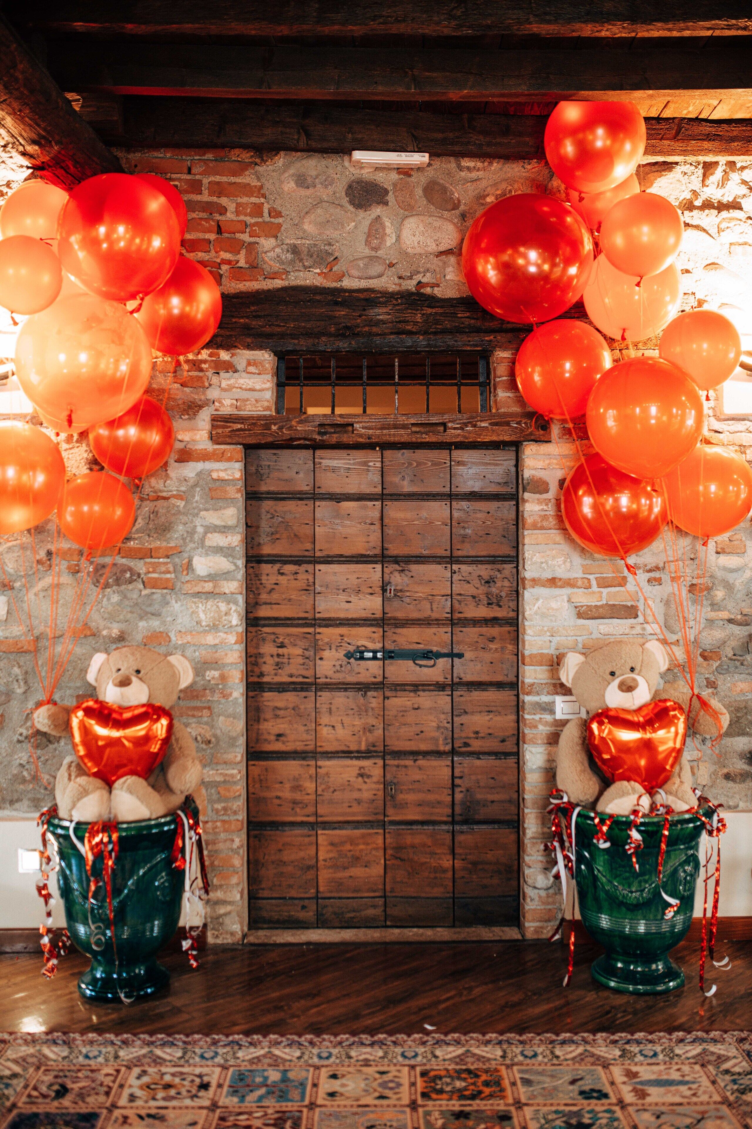 Um quarto rústico com porta de madeira, dois vasos em formato de urso com fitas vermelhas e uma parede de tijolos.