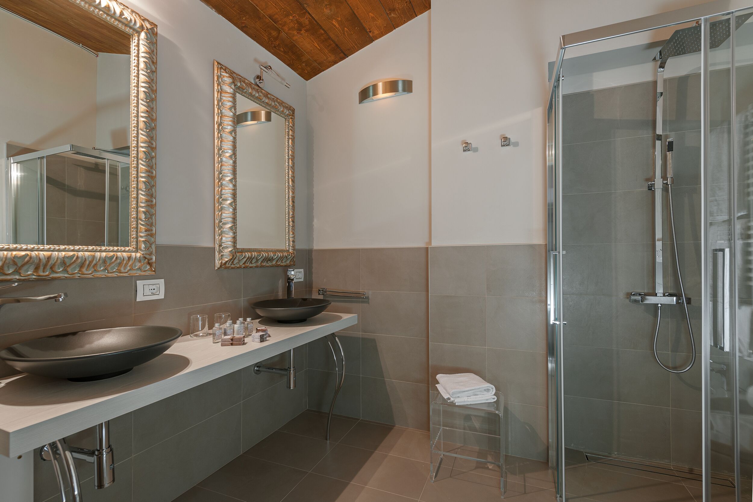 A modern bathroom with a large mirror, a vessel sink, a glass shower enclosure, and a clear stool.