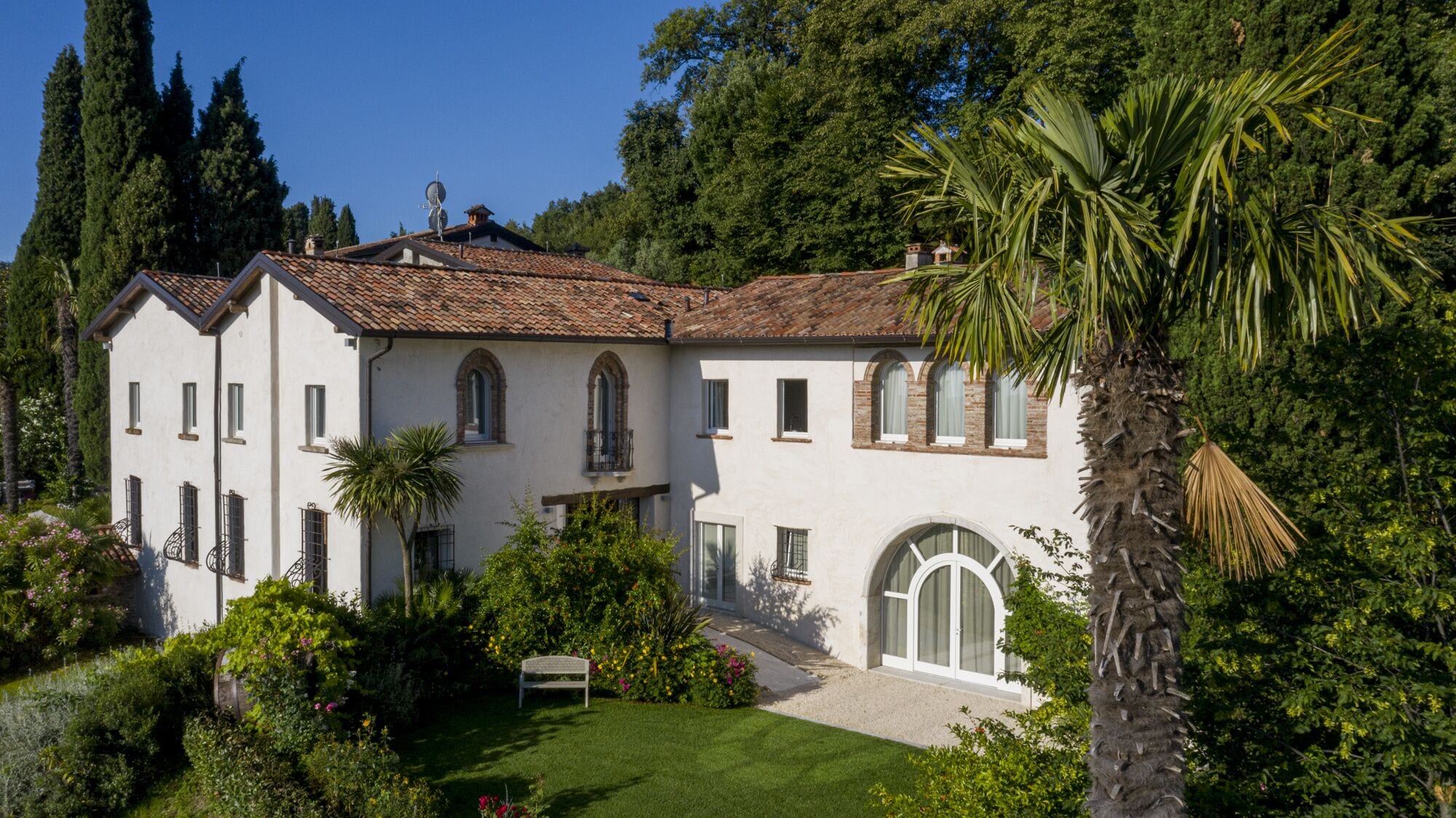 Une villa blanche, dotée d’un toit en tuiles, entourée d’une végétation luxuriante et d’un jardin bien entretenu.