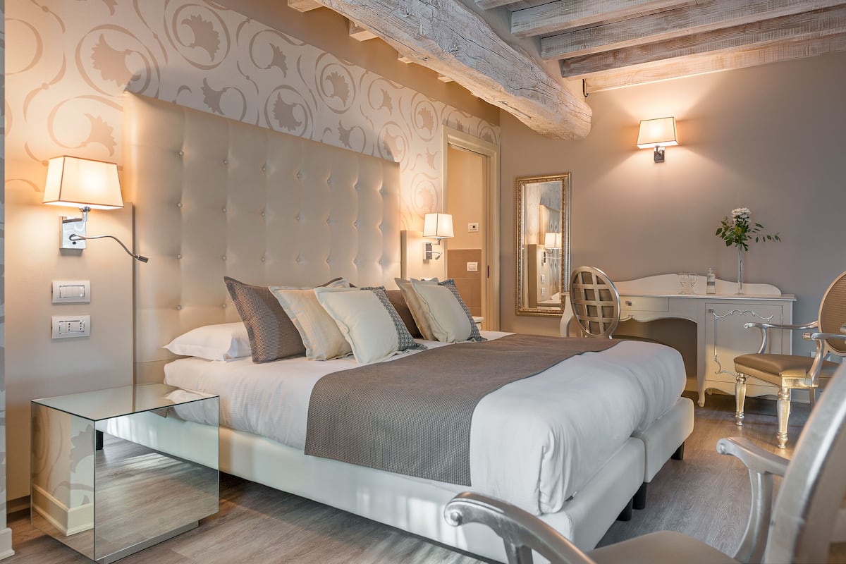 A modern bedroom with a tufted headboard, a glass bedside table, a desk with a chair, and a mirror.