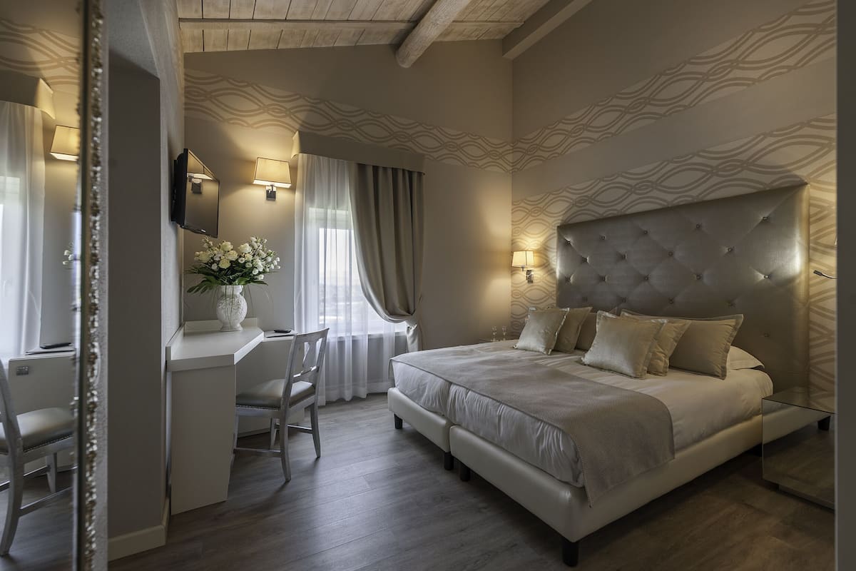 A bedroom with a large bed, a desk with a chair, a mirror, and a wall-mounted TV.