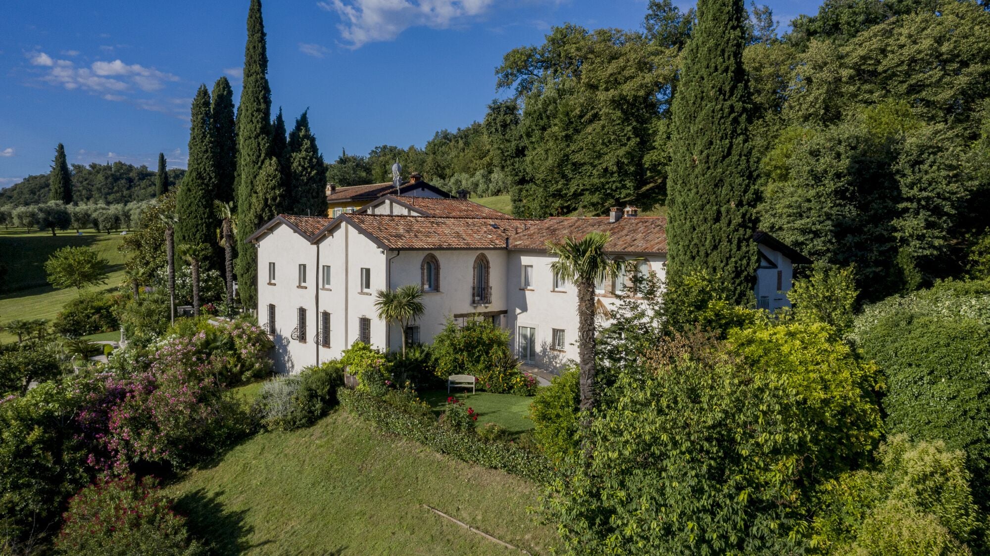 A large, two-story building with a tiled roof, surrounded by lush greenery and trees.
