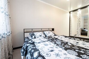 A bedroom with a bed, a large mirror, and a window with sheer curtains.