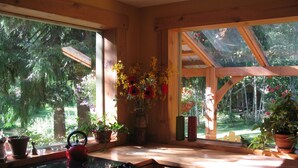A kitchen with wooden cabinets, a stove, and a window overlooking a garden with potted plants and flowers. - Kaslo Getaway - private and natural experience. (Kaslo)